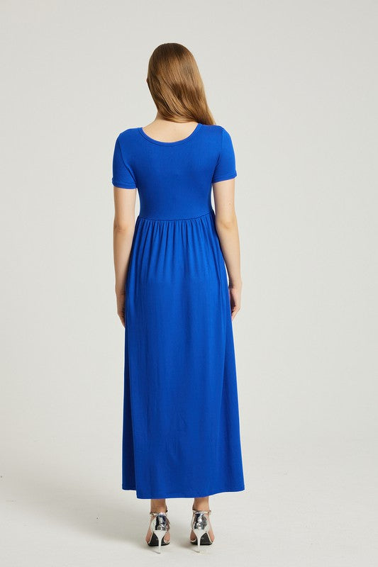 A woman in a blue Women's Summer Casual Maxi Dress With Pocket sits on a white chair. The short sleeve design complements her look as she gazes at the camera with a neutral expression.