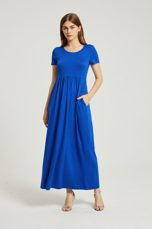 A woman in a blue Women's Summer Casual Maxi Dress With Pocket sits on a white chair. The short sleeve design complements her look as she gazes at the camera with a neutral expression.
