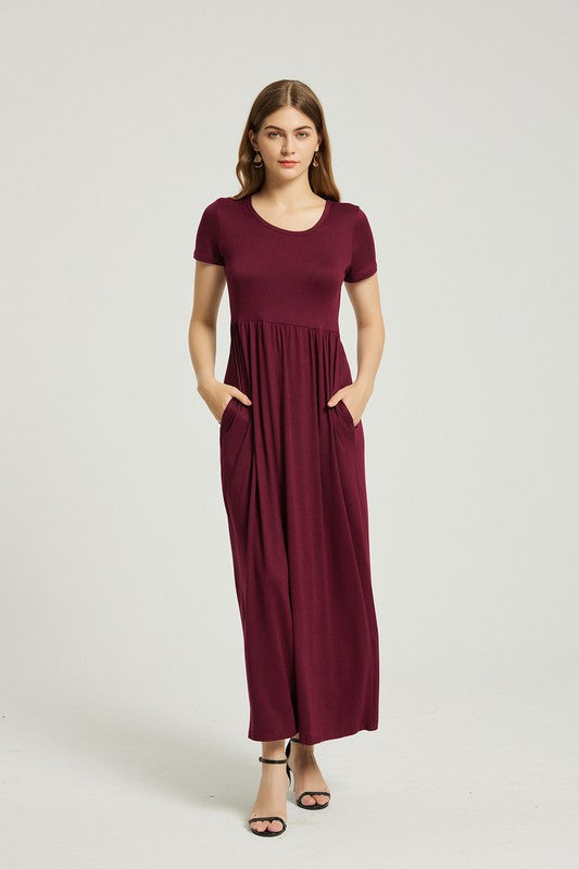 A woman wearing the Women's Summer Casual Maxi Dress With Pocket in burgundy sits on a wooden chair, resting her arm on its back. She has long brown hair and is sporting black high heel sandals.