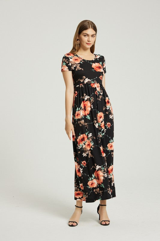 A woman sits in a modern wooden chair, wearing the stylish Womens Summer Casual Floral Maxi Dress With Pocket and matching floral heels, with her right hand resting on her chin and her left arm on her lap.