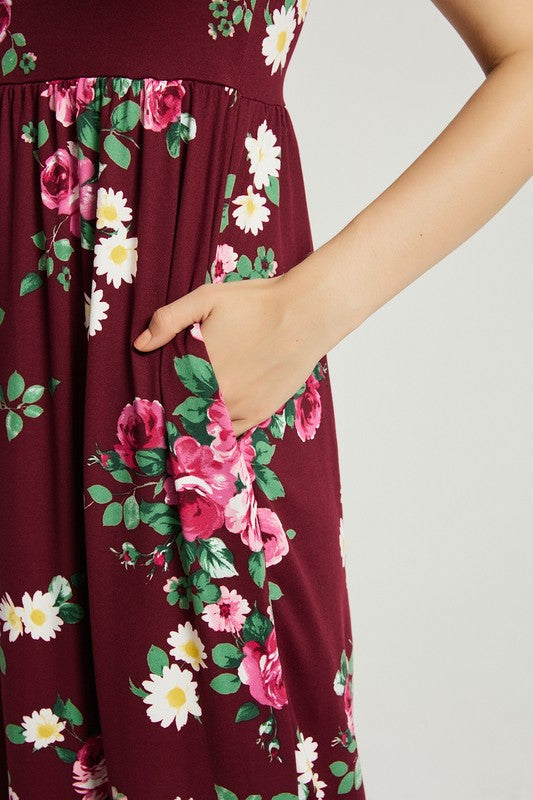 A woman sits in a wooden chair wearing a Womens Summer Casual Floral Maxi Dress With Pocket and black heels, with her left elbow resting on the armrest and her left hand touching her chin.