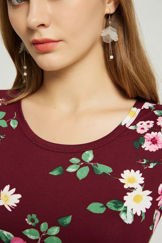 A woman wearing the Womens Summer Casual Floral Maxi Dress With Pocket in black floral is sitting on a modern wooden chair, resting her chin on her left hand and looking at the camera.