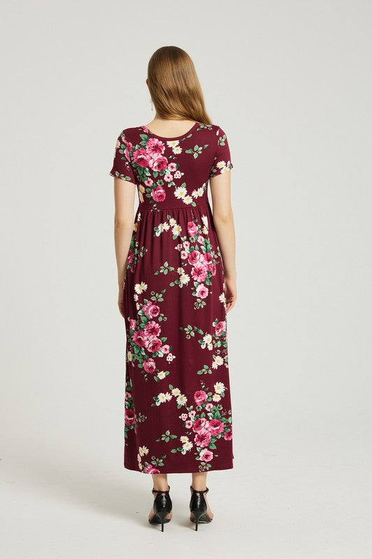 A woman in a Women's Summer Casual Floral Maxi Dress With Pocket is seated on a modern wooden chair with her hand resting on her chin, looking straight ahead.