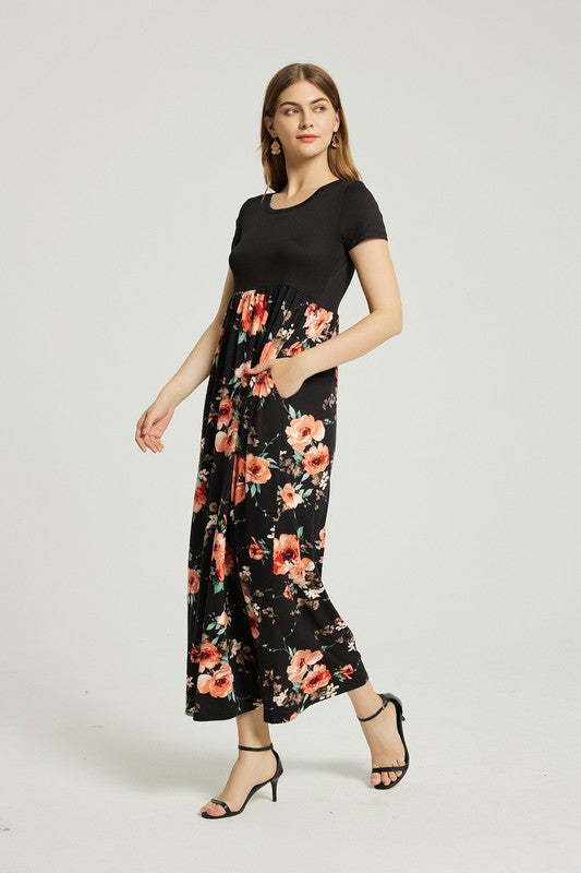 A woman stands with hands in pockets, wearing a Women's Summer Casual Floral Maxi Dress With Pocket featuring black and red floral patterns. She has long hair and is sporting black heeled sandals.