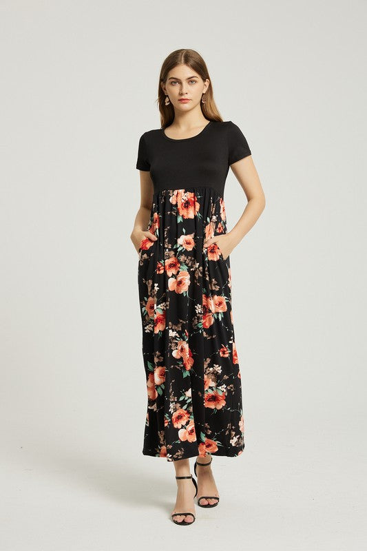 A woman stands with hands in pockets, wearing a Women's Summer Casual Floral Maxi Dress With Pocket featuring black and red floral patterns. She has long hair and is sporting black heeled sandals.