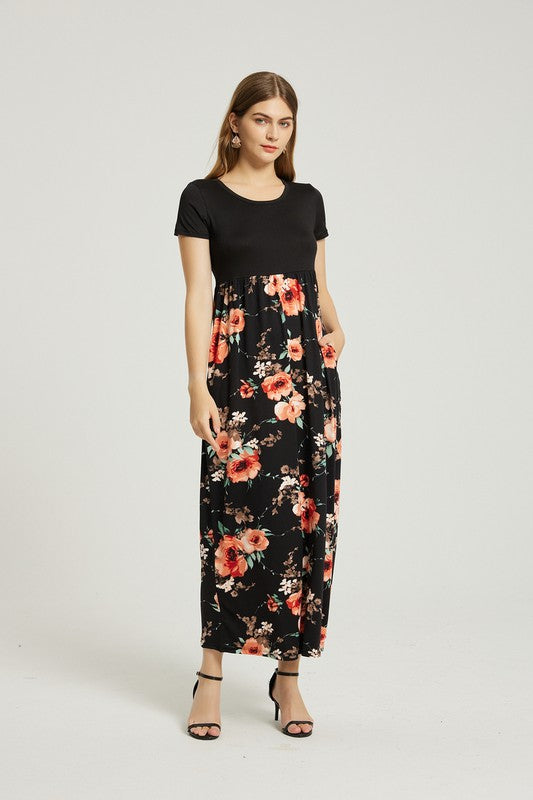 A woman stands with hands in pockets, wearing a Women's Summer Casual Floral Maxi Dress With Pocket featuring black and red floral patterns. She has long hair and is sporting black heeled sandals.
