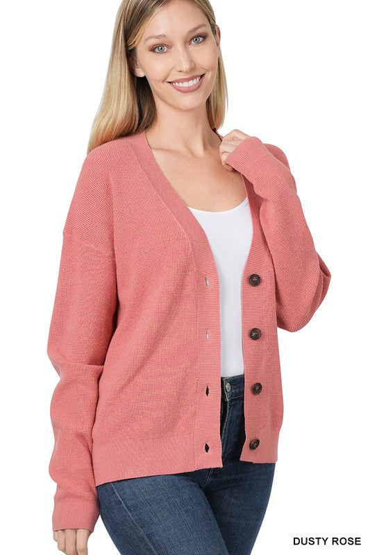 Two views of a woman wearing the Viscose Sweater Cardigan in dusty blush, featuring black button-front closure over a white top and blue jeans. The front view displays her smiling, while the back view highlights the drop shoulder design and cardigan's texture.