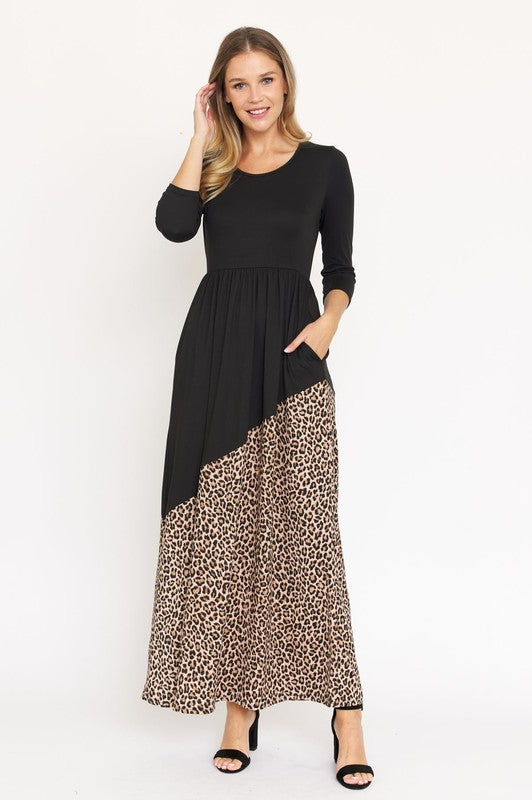 A woman wearing an Asymmetrical Leopard Accent Maxi Dress, made from polyester and featuring convenient pockets, stands against a plain white background.