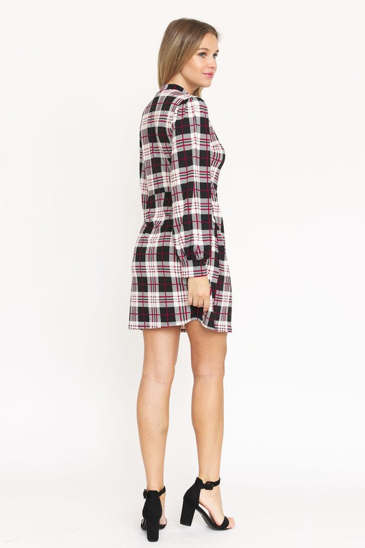 A woman stands smiling, wearing the High Neck Plaid Sheath Dress featuring a classic United States style in black, white, and red plaid with long sleeves.