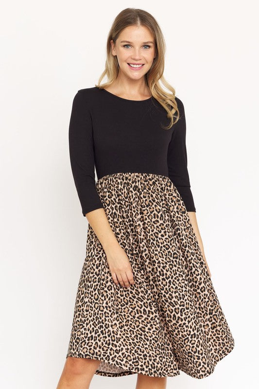 A woman is wearing a stunning Quarter Sleeve Midi Dress featuring a bold leopard print. Standing against a white background, she smiles effortlessly. Proudly made in the United States, this dress perfectly combines elegance and boldness.