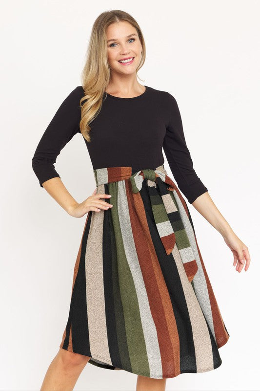 Woman in a neutral-toned room wearing a Quarter Sleeve Stripe Sash Midi Dress, standing near beige dried plants.