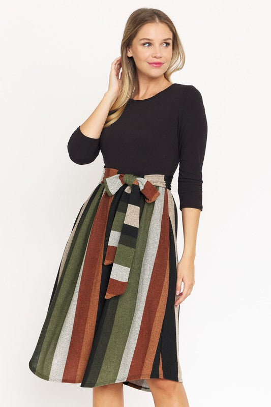 Woman in a neutral-toned room wearing a Quarter Sleeve Stripe Sash Midi Dress, standing near beige dried plants.