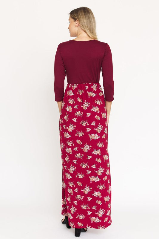 A person is wearing the Quarter Sleeve Floral Maxi Dress in burgundy, featuring a fitted top and a flowing skirt adorned with a delicate floral pattern. This dress, made from a blend of polyester and spandex, has convenient pockets. They have paired it with black sandals.