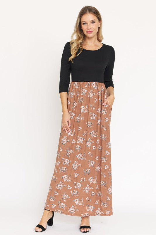 A person is wearing the Quarter Sleeve Floral Maxi Dress in burgundy, featuring a fitted top and a flowing skirt adorned with a delicate floral pattern. This dress, made from a blend of polyester and spandex, has convenient pockets. They have paired it with black sandals.