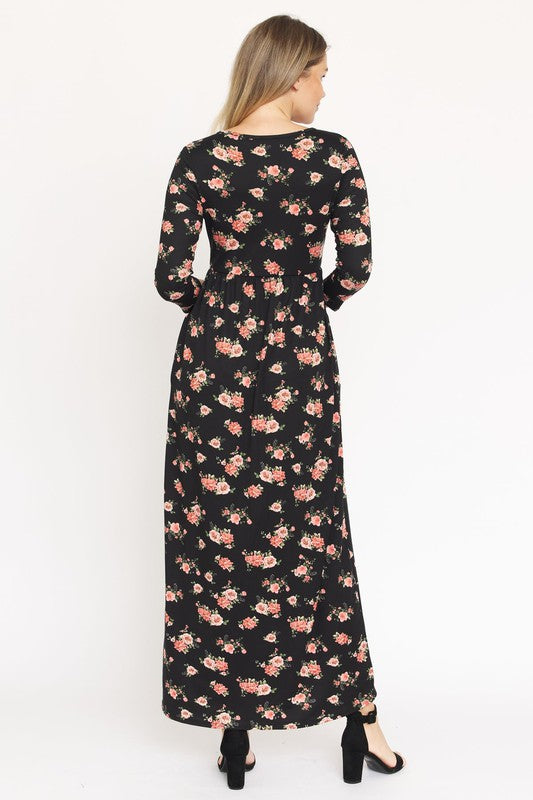 A woman in the Bouquet Floral Quarter Sleeve Maxi Dress poses against a plain white background. She is standing with one hand touching her hair and wearing black heels, showcasing the elegance of her U.S.-made black floral maxi dress.