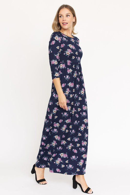 A woman stands wearing a dark blue Plus Bouquet Floral Quarter Sleeve Maxi Dress with black heels, against a plain white background.