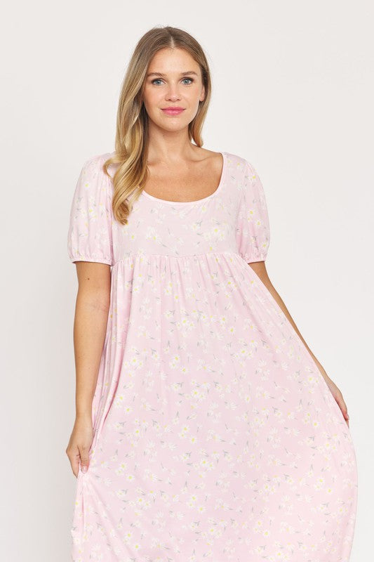 A woman is wearing the Empire Waist Floral Puff Sleeve Dress, which is light pink with an ankle-length cut and features a floral pattern. The dress includes short, floral puff sleeves. She completes her outfit with white sneakers and stands against a plain white background.