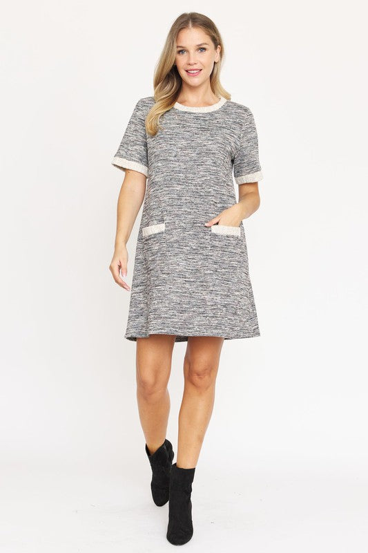 A woman with long blonde hair models the short-sleeved Preppy Tweed Shift Dress in gray and white, featuring two front pockets. She stands against a plain white background, smiling at the camera.