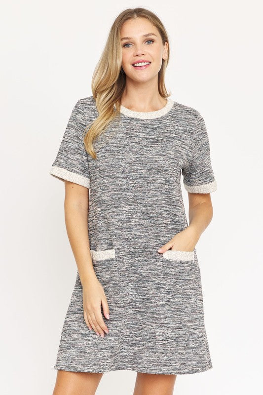 A woman with long blonde hair models the short-sleeved Preppy Tweed Shift Dress in gray and white, featuring two front pockets. She stands against a plain white background, smiling at the camera.