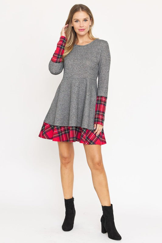 A woman stands facing forward wearing a Terry Plaid Layered Fit And Flare Dress, a long-sleeve grey number with red plaid accents on the sleeves and hem.