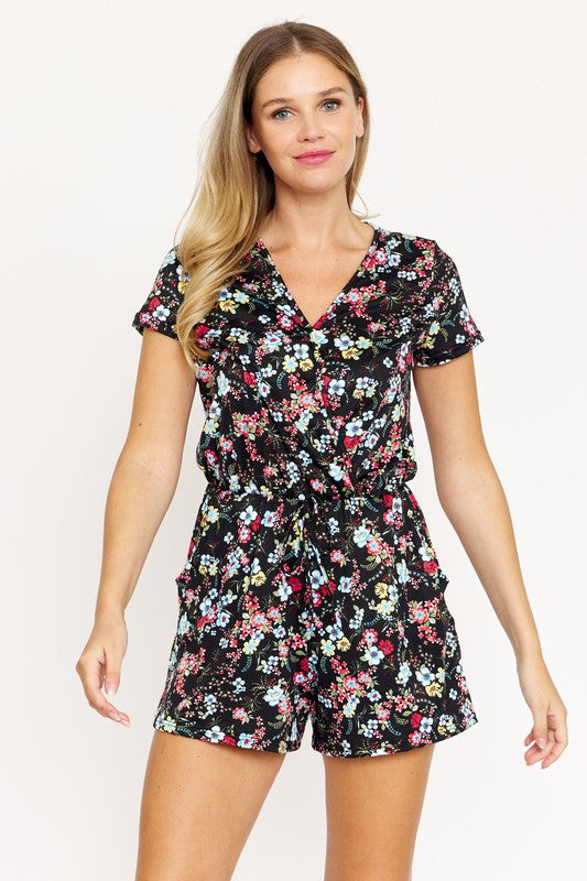 A woman is smiling at the camera, wearing a stylish Surplice Drawstring Floral Romper with short sleeves and a V-neckline.