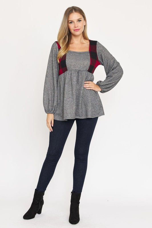 A person with long hair is standing, wearing a grey long-sleeved Terry Plaid Side Contrast Baby Doll Tunic featuring black and red plaid details, along with dark pants against a plain white background.