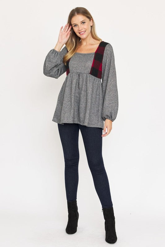 A person with long hair is standing, wearing a grey long-sleeved Terry Plaid Side Contrast Baby Doll Tunic featuring black and red plaid details, along with dark pants against a plain white background.