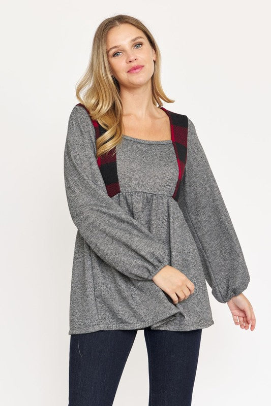 A person with long hair is standing, wearing a grey long-sleeved Terry Plaid Side Contrast Baby Doll Tunic featuring black and red plaid details, along with dark pants against a plain white background.