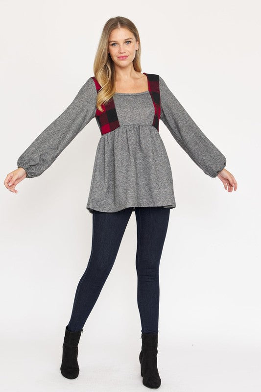 A person with long hair is standing, wearing a grey long-sleeved Terry Plaid Side Contrast Baby Doll Tunic featuring black and red plaid details, along with dark pants against a plain white background.