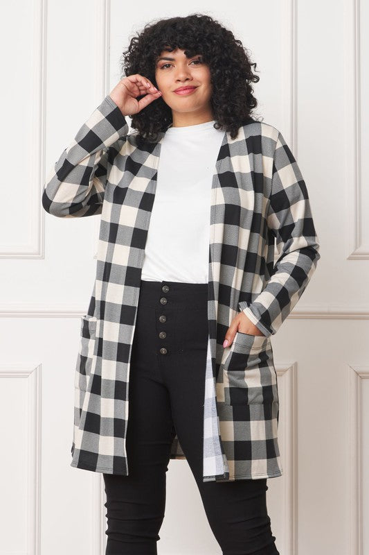 A woman in a Long Buffalo Plaid Open Cardigan, featuring a striking red design and crafted from soft polyester spandex, stands against a plain background. She pairs it with a white top and dark jeans, facing the camera with her hands in front pockets. Made in the United States, this look combines comfort and style effortlessly.