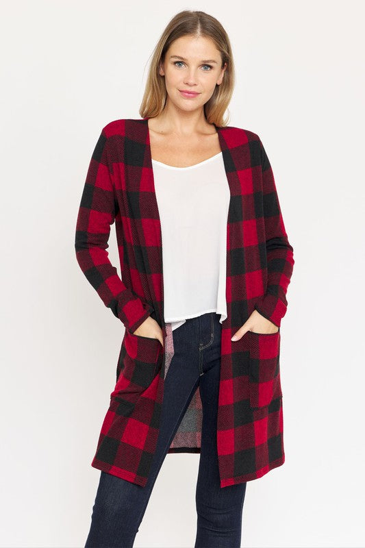 A woman stands against a plain background, wearing a red and black checkered Long Buffalo Plaid Open Cardigan over a white top and dark jeans.