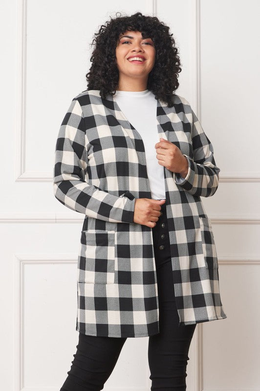 A woman in a Long Buffalo Plaid Open Cardigan, featuring a striking red design and crafted from soft polyester spandex, stands against a plain background. She pairs it with a white top and dark jeans, facing the camera with her hands in front pockets. Made in the United States, this look combines comfort and style effortlessly.