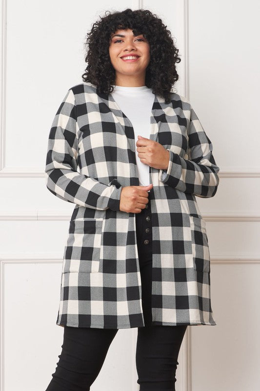 A woman stands against a plain background, wearing a red and black checkered Long Buffalo Plaid Open Cardigan over a white top and dark jeans.