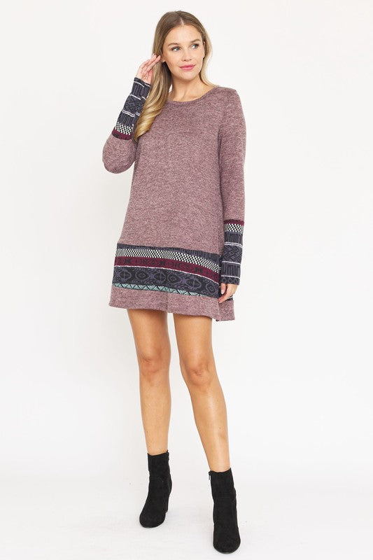 A woman wearing the Plus Nordic Print Knit Dress, featuring green long sleeves with Nordic print cuffs and hem, smiles as she touches her hair.