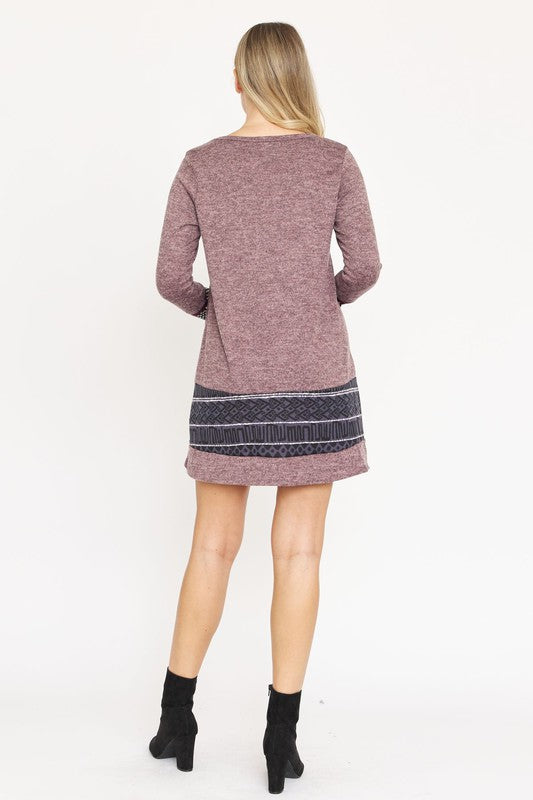 A woman in a maroon Nordic Print Knit Dress, featuring intricate patterned bands at the hem and cuffs, smiles at the camera against a plain white background.