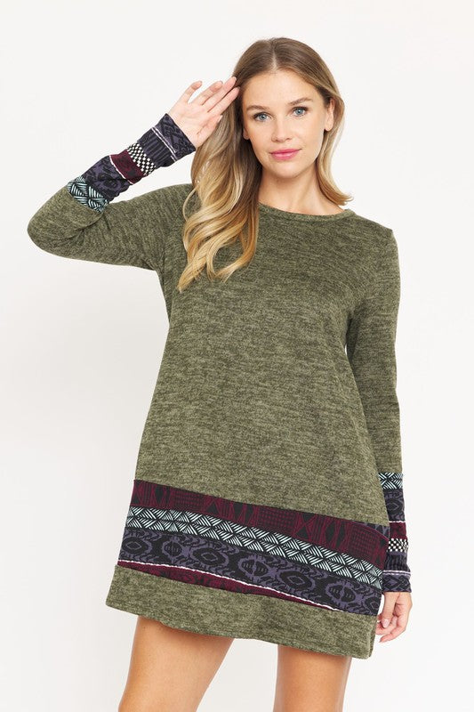 A woman wearing the Plus Nordic Print Knit Dress, featuring green long sleeves with Nordic print cuffs and hem, smiles as she touches her hair.