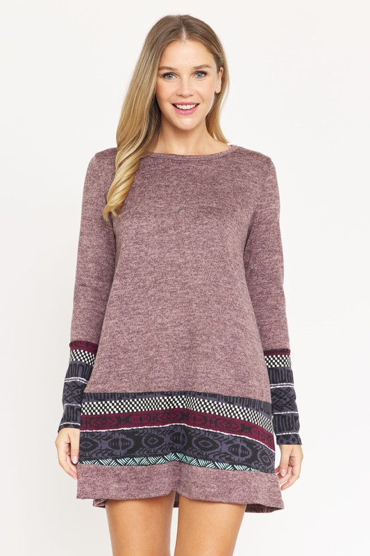 A woman wearing the Plus Nordic Print Knit Dress, featuring green long sleeves with Nordic print cuffs and hem, smiles as she touches her hair.