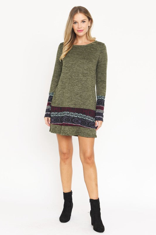 A woman wearing the Plus Nordic Print Knit Dress, featuring green long sleeves with Nordic print cuffs and hem, smiles as she touches her hair.