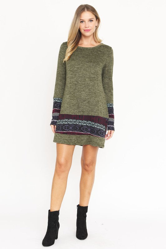 A woman wearing the Plus Nordic Print Knit Dress, featuring green long sleeves with Nordic print cuffs and hem, smiles as she touches her hair.