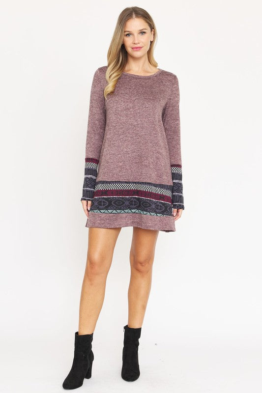 A woman in a maroon Nordic Print Knit Dress, featuring intricate patterned bands at the hem and cuffs, smiles at the camera against a plain white background.