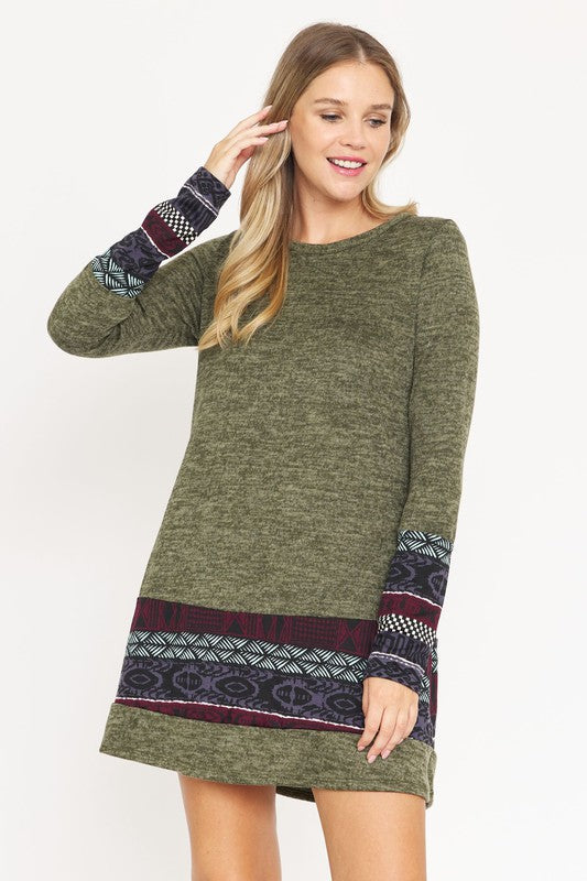 A woman wearing the Plus Nordic Print Knit Dress, featuring green long sleeves with Nordic print cuffs and hem, smiles as she touches her hair.