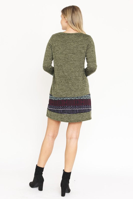 A woman wearing the Plus Nordic Print Knit Dress, featuring green long sleeves with Nordic print cuffs and hem, smiles as she touches her hair.