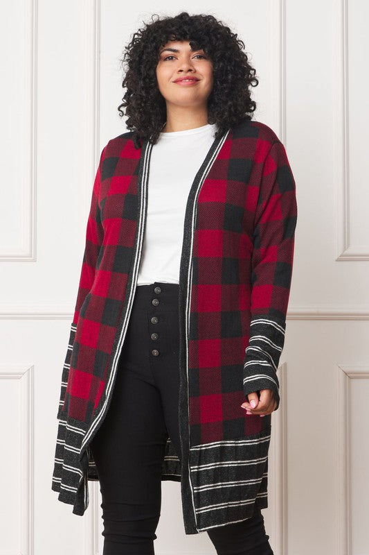 A person with curly hair is wearing a Long Buffalo Plaid Stripe Trim Open Cardigan in black and white over a white shirt, paired with black high-waisted pants with buttons. They stand in front of a white paneled wall.