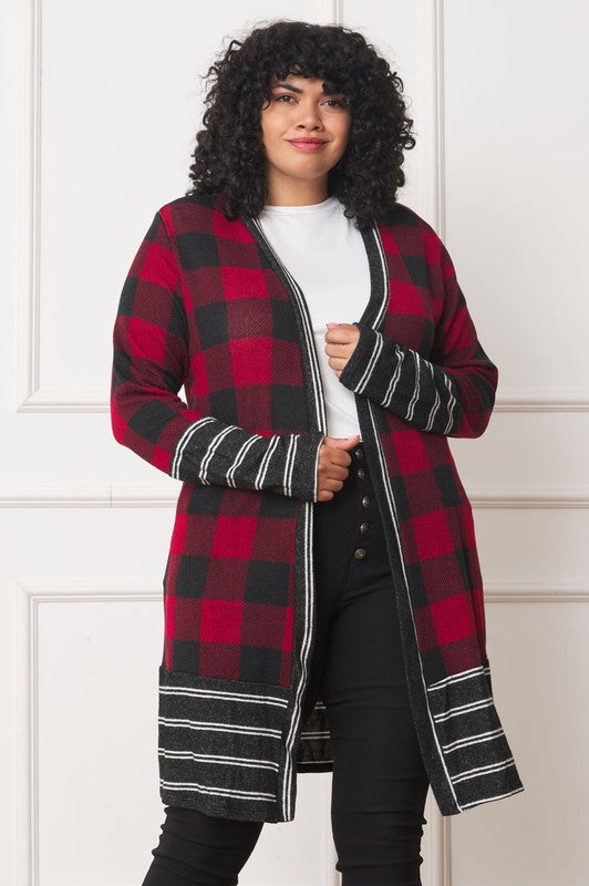 A person with curly hair is wearing a Long Buffalo Plaid Stripe Trim Open Cardigan in black and white over a white shirt, paired with black high-waisted pants with buttons. They stand in front of a white paneled wall.