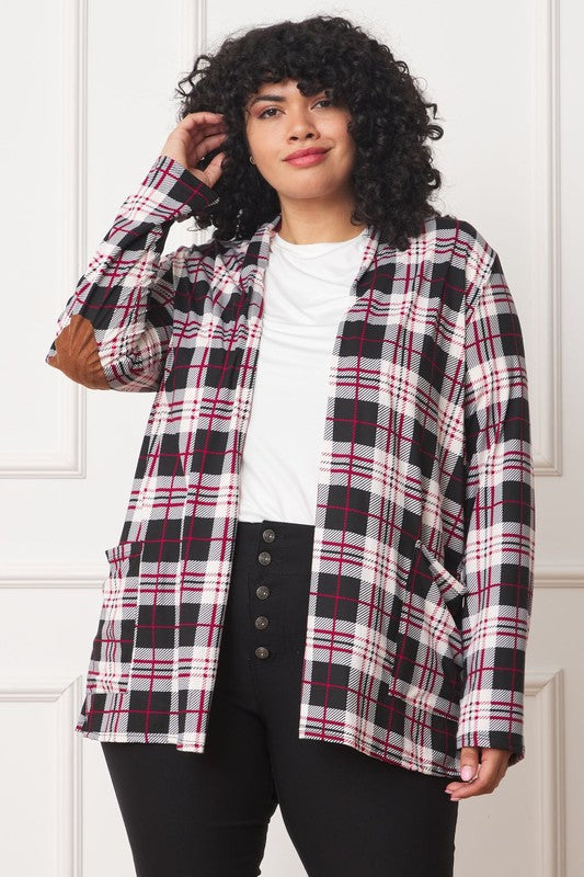 A woman with curly hair is standing against a white background, wearing a white shirt, black pants, and a Plaid Contrast Elbow Patch Cardigan made in the United States.