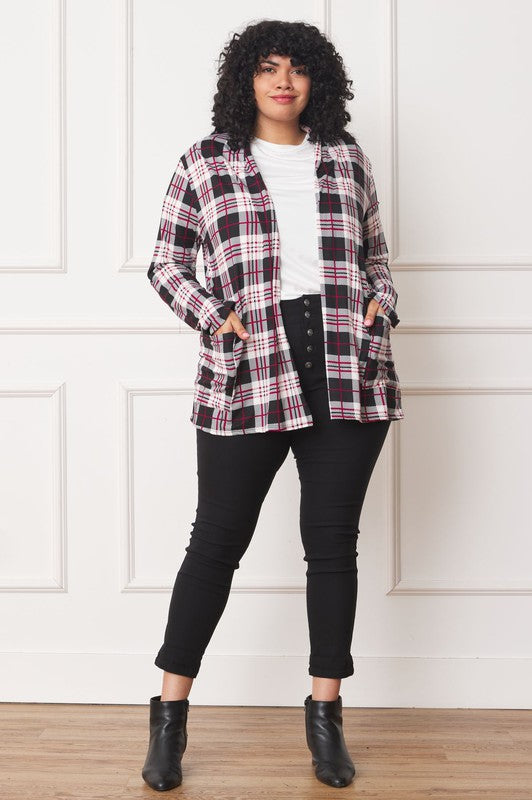 A woman with curly hair is standing against a white background, wearing a white shirt, black pants, and a Plaid Contrast Elbow Patch Cardigan made in the United States.