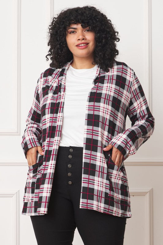 A woman with curly hair is standing against a white background, wearing a white shirt, black pants, and a Plaid Contrast Elbow Patch Cardigan made in the United States.