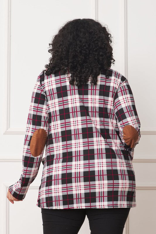 A woman with curly hair is standing against a white background, wearing a white shirt, black pants, and a Plaid Contrast Elbow Patch Cardigan made in the United States.