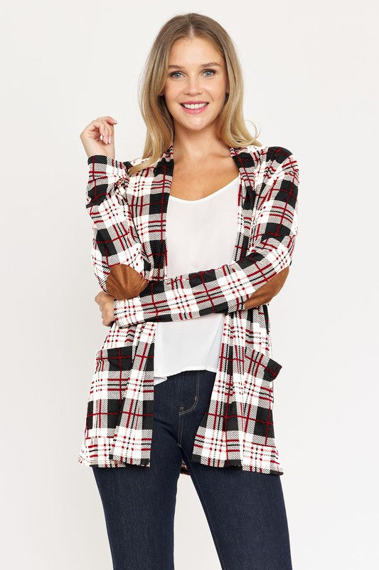 A woman with curly hair is standing against a white background, wearing a white shirt, black pants, and a Plaid Contrast Elbow Patch Cardigan made in the United States.