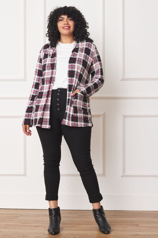 A woman with curly hair is standing against a white background, wearing a white shirt, black pants, and a Plaid Contrast Elbow Patch Cardigan made in the United States.